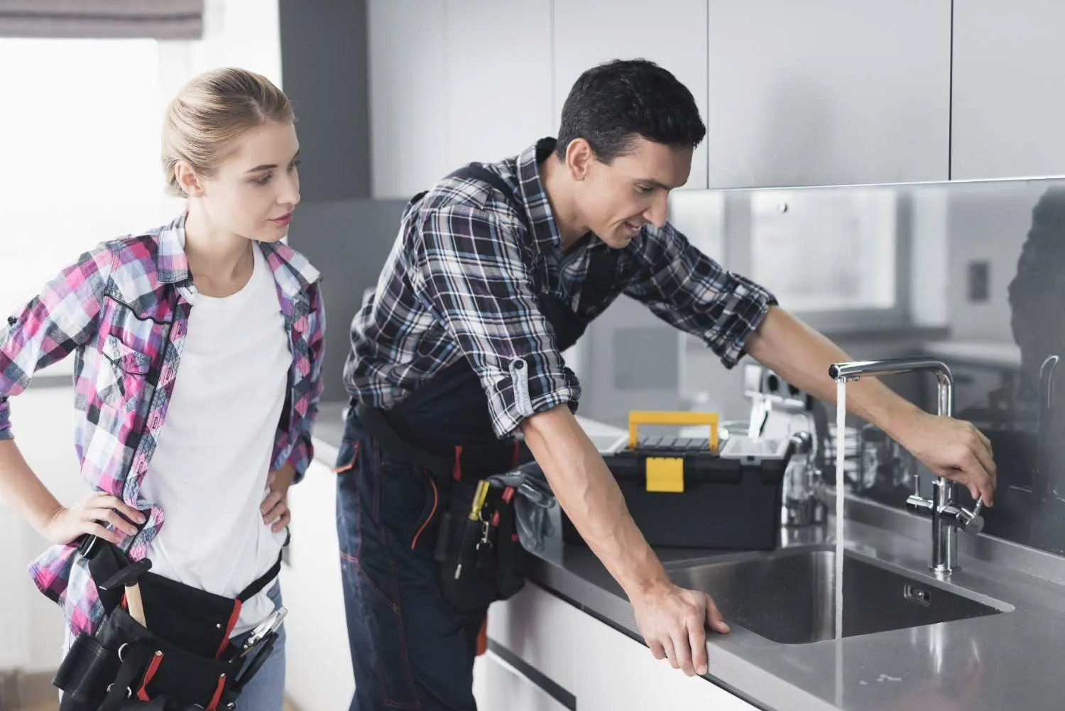 Technician checking a kitchen faucet while the homeowner watches